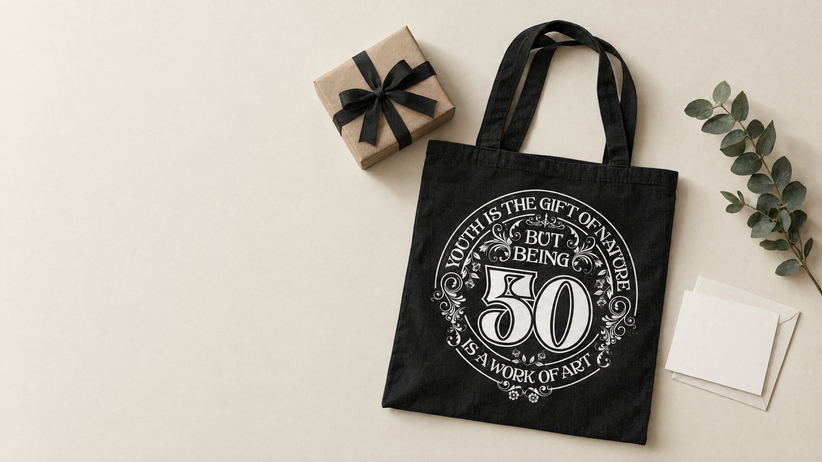 Black 50th birthday tote bag with Youth is the Gift of Nature print beside a kraft paper gift and a blank card