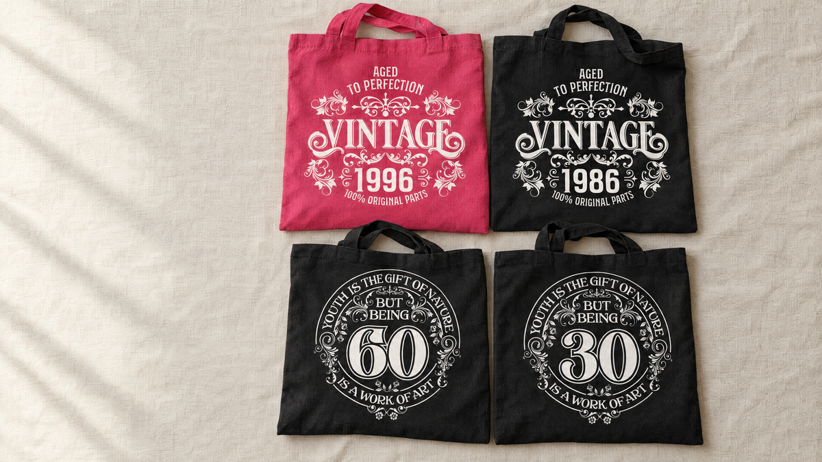 Four birthday tote bags on linen: pink Vintage 1996, black Vintage 1986 and Being 60 and Being 30 designs