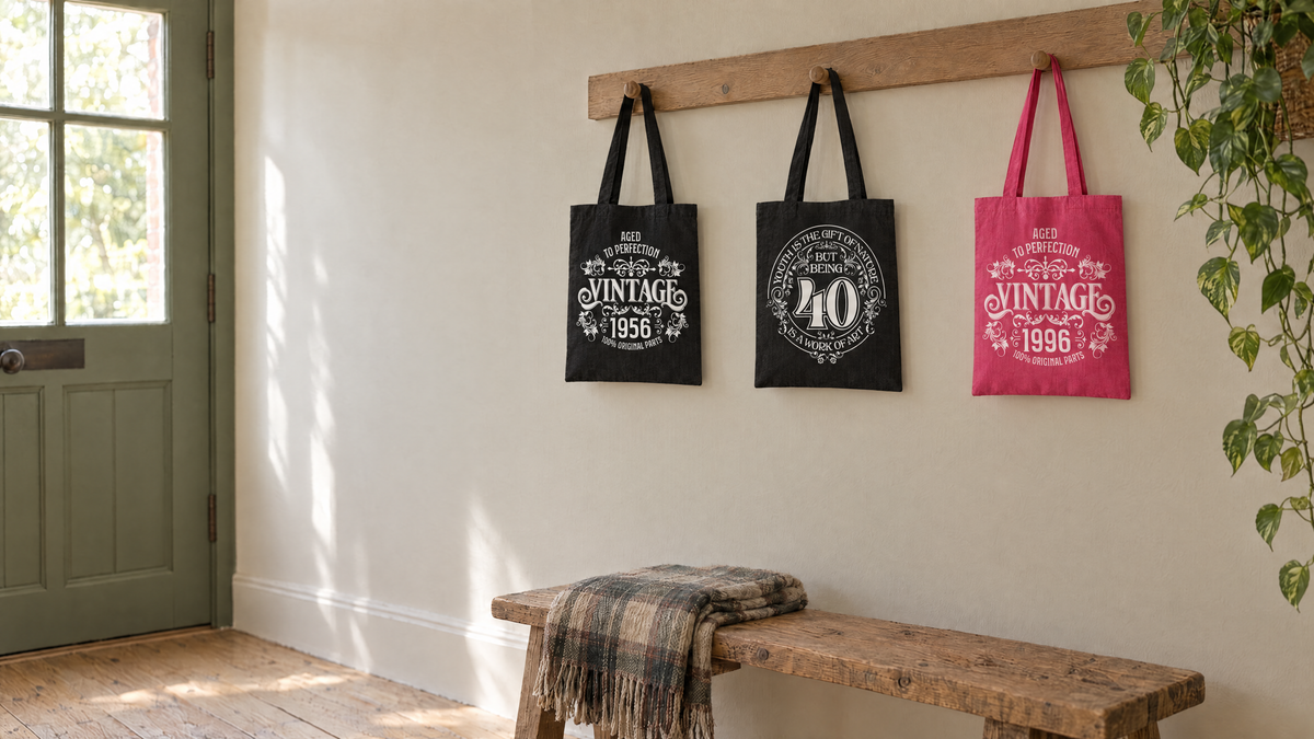 Three birthday tote bags on wooden hooks in a bright hallway: Vintage 1956, Being 40 and pink Vintage 1996 designs