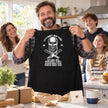 Man holding up his new skull BBQ apron gift with family in the kitchen